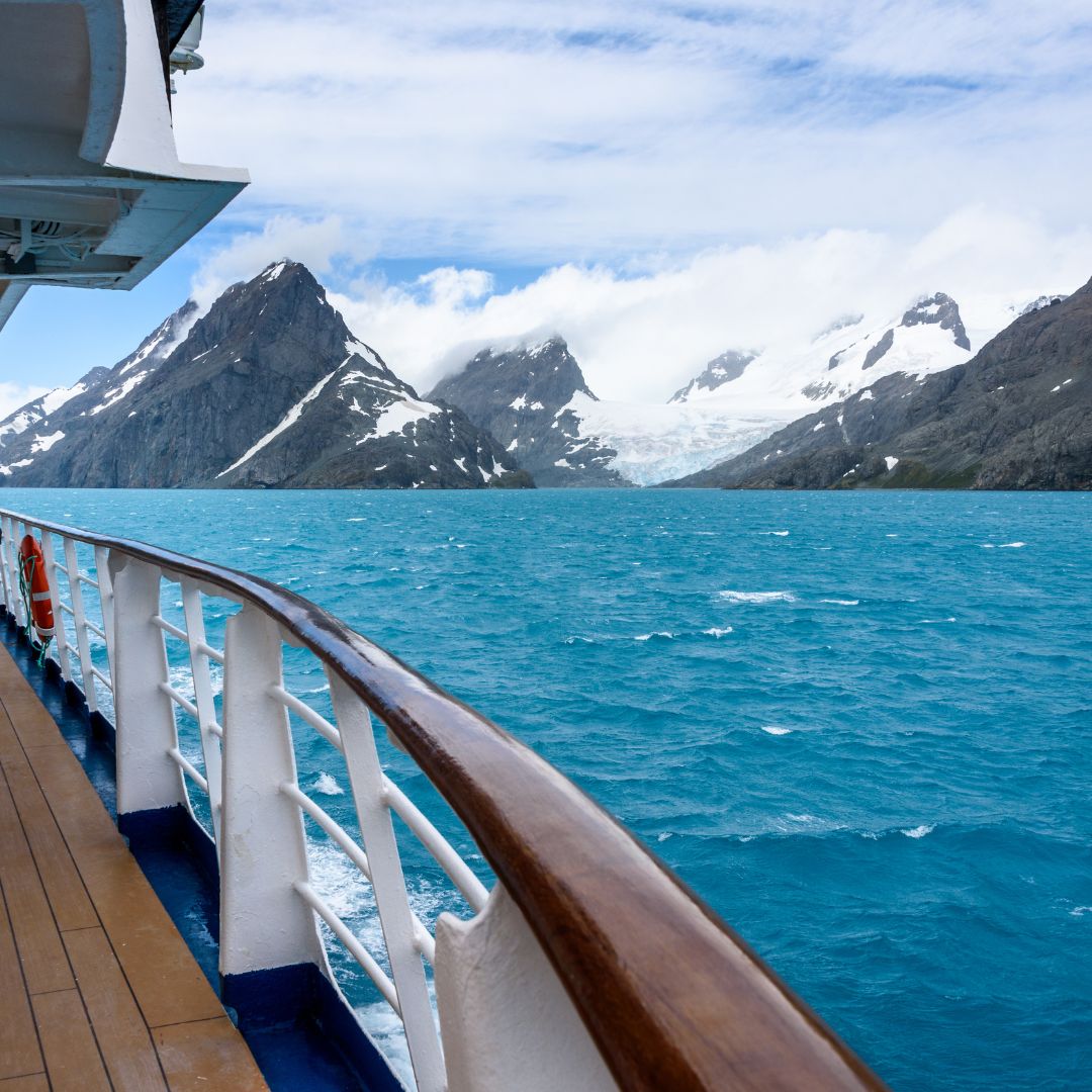 Cruise ship deck overlooking a sea with snowy mountains in the background.